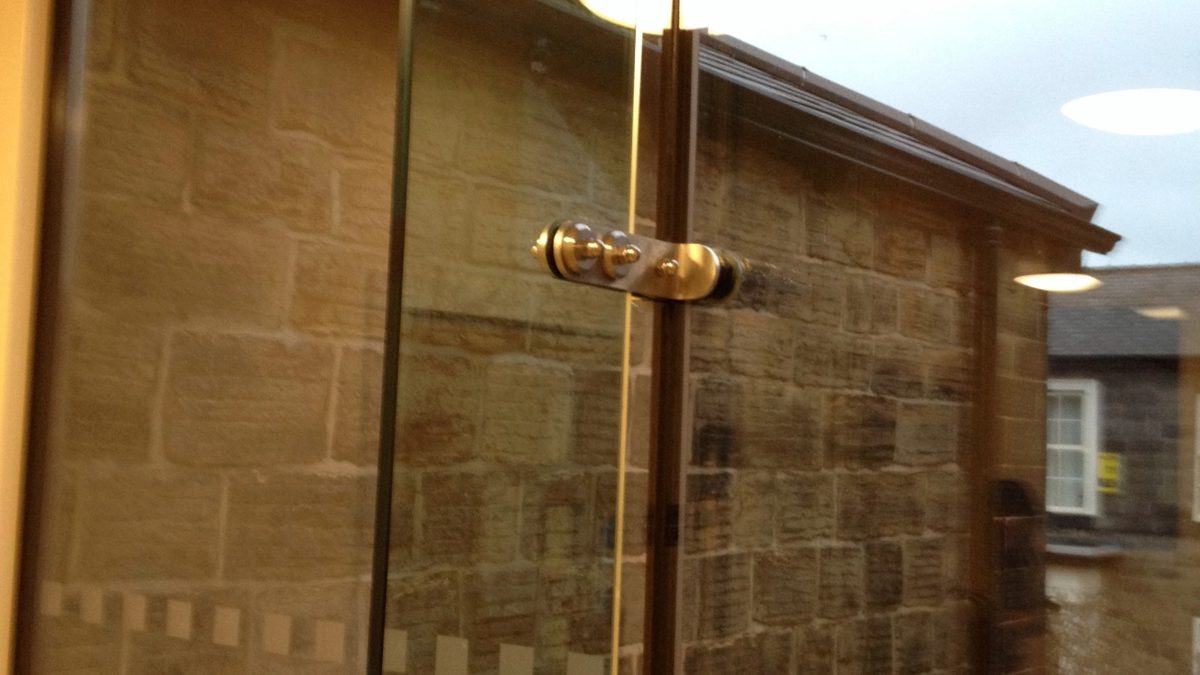 Point-fixed glass panel with spacer fitting against stone façade